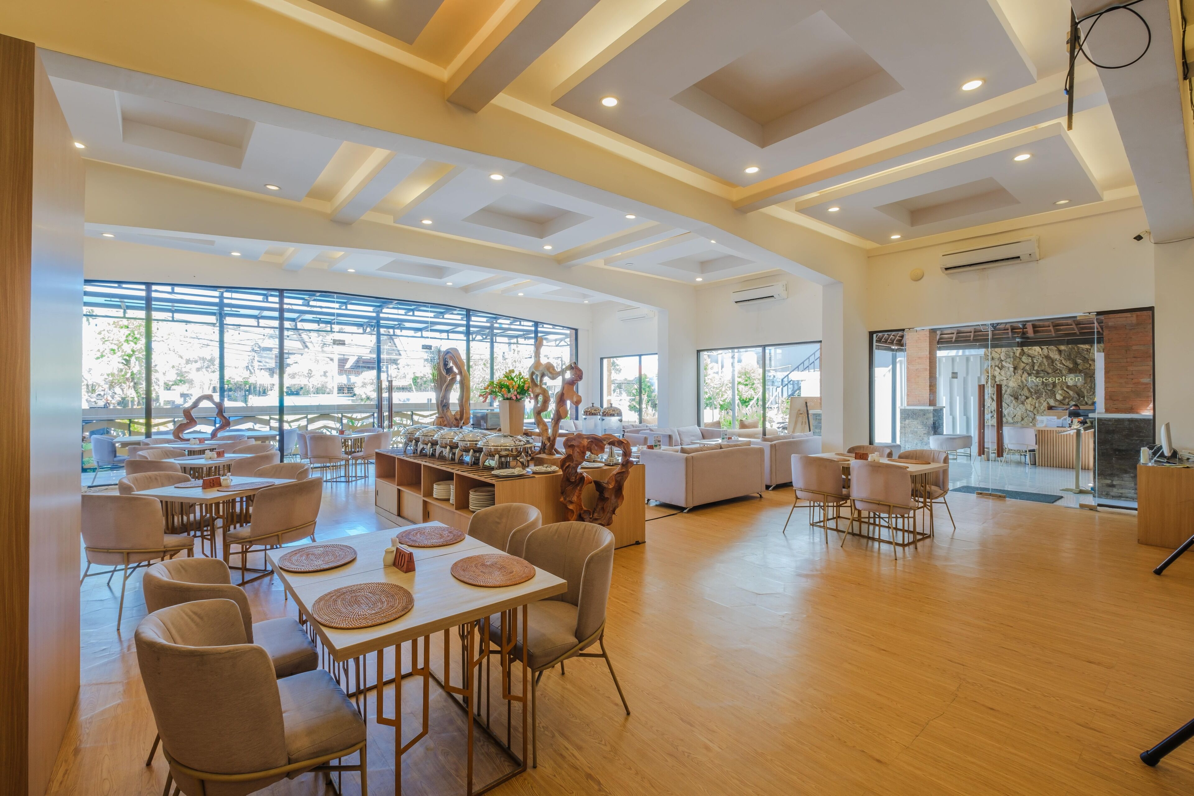 A spacious hotel lobby with multiple seating areas, a reception desk, and large windows offering views of the outdoors.