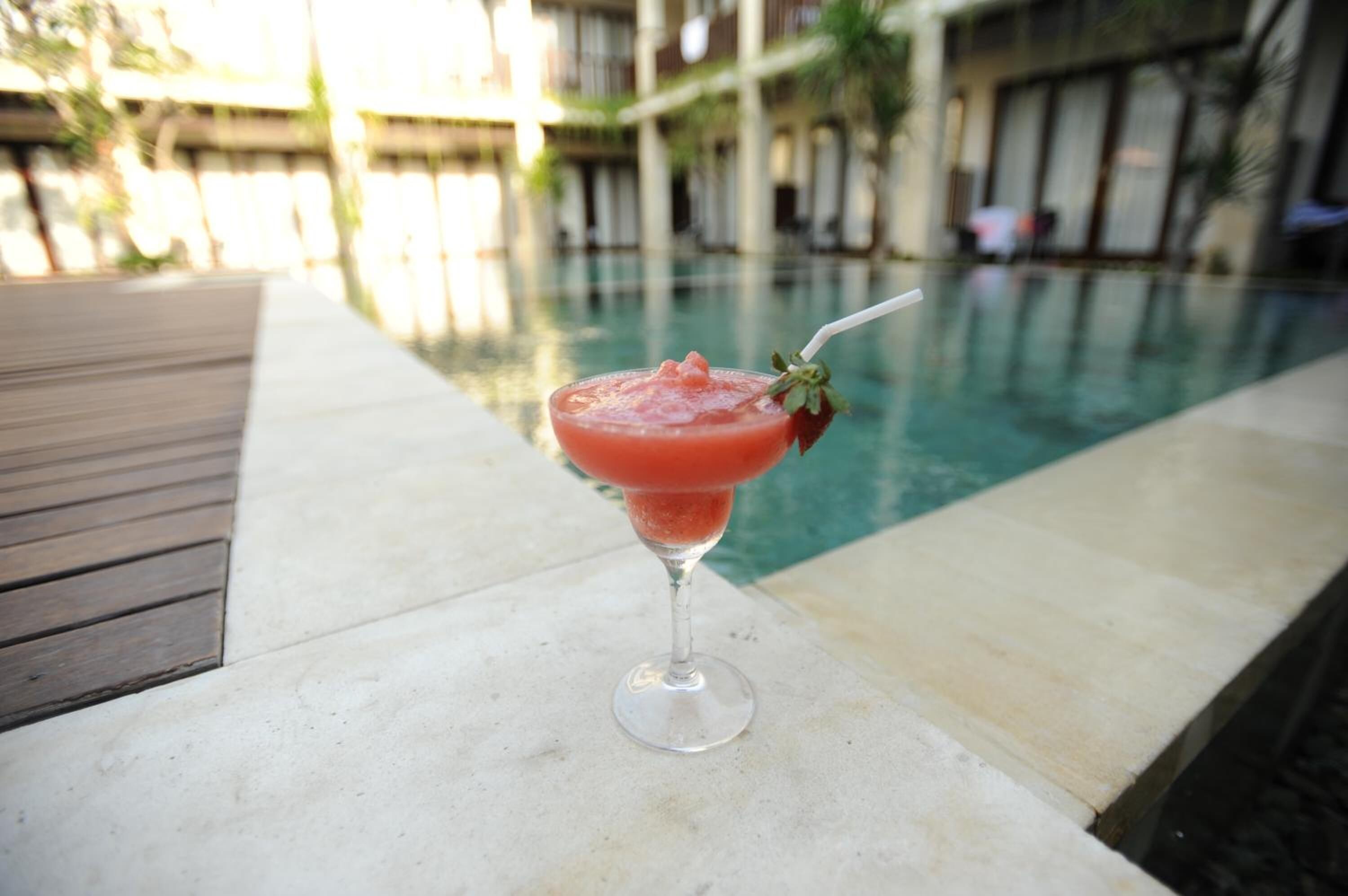 A cocktail on a poolside table with a pool and hotel buildings in the background.
