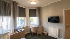 A room with a desk, chair, TV, radiator, and a window with curtains. - Smartsway Hotel & Wellness (Eastbourne)