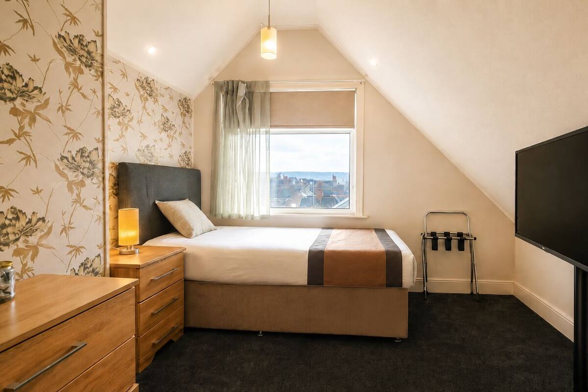A bedroom with a bed, a TV, a window, a dresser, and a lamp.