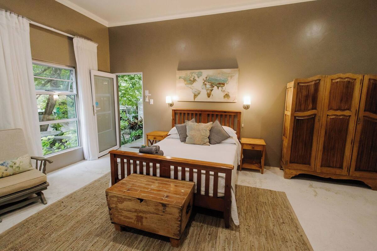 A bedroom with a bed, wooden wardrobe, and a view of greenery through a sliding door.