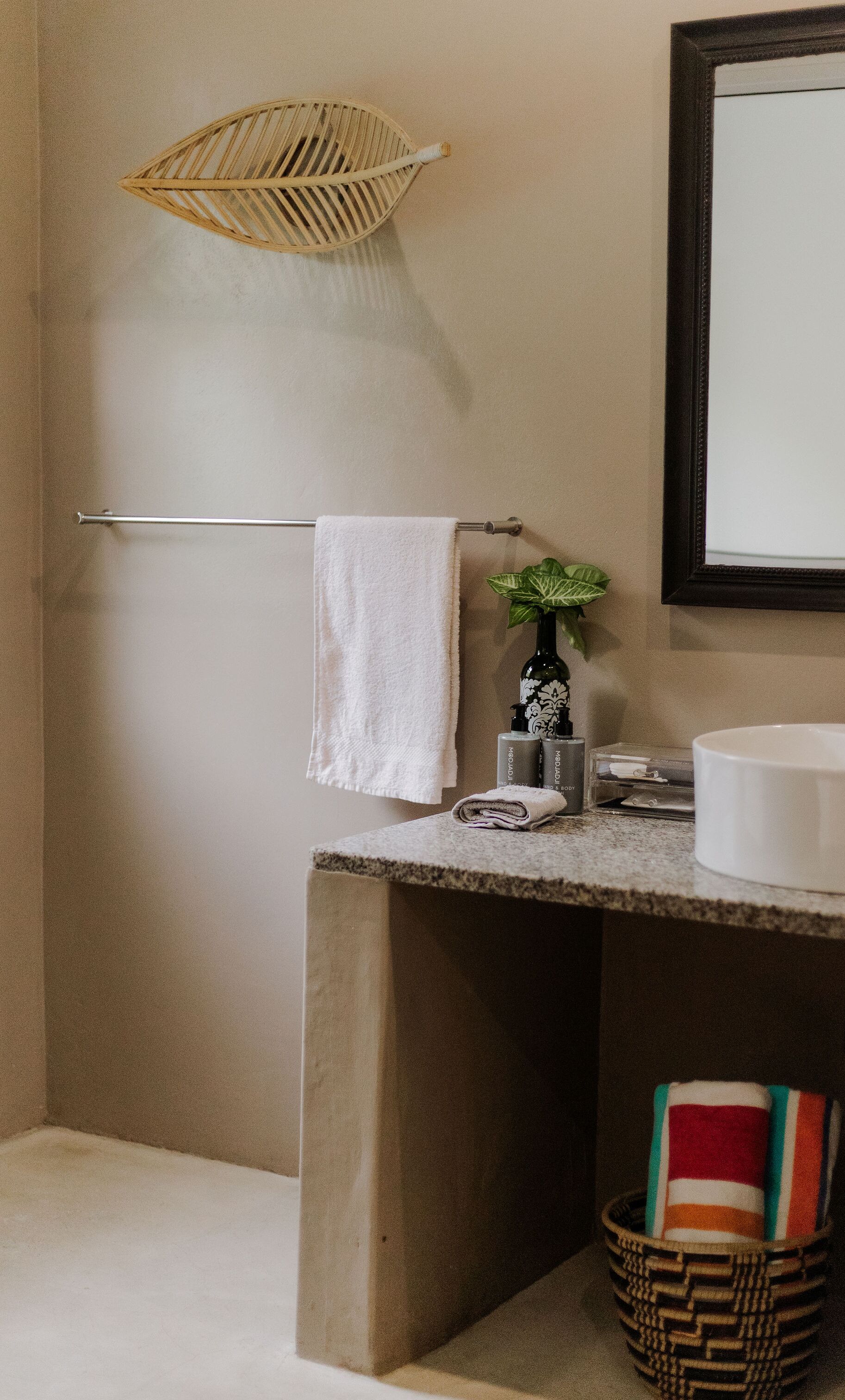 A bathroom with a white sink, a towel rack, a decorative plant, and a woven basket.
