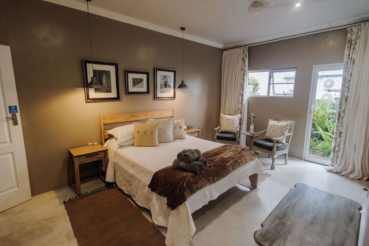A bedroom with a large bed, a wooden nightstand, a chair, and a window with curtains.