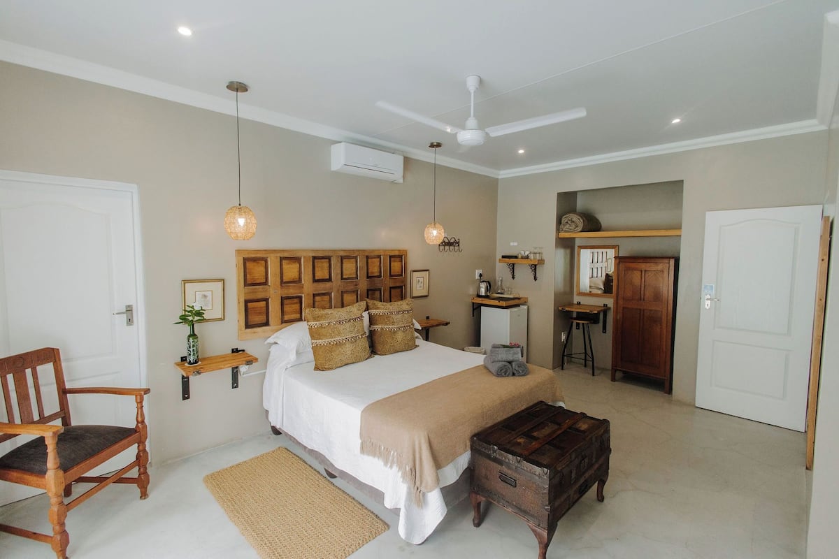 A bedroom with a large bed, a wooden chair, a small table, and a ceiling fan.