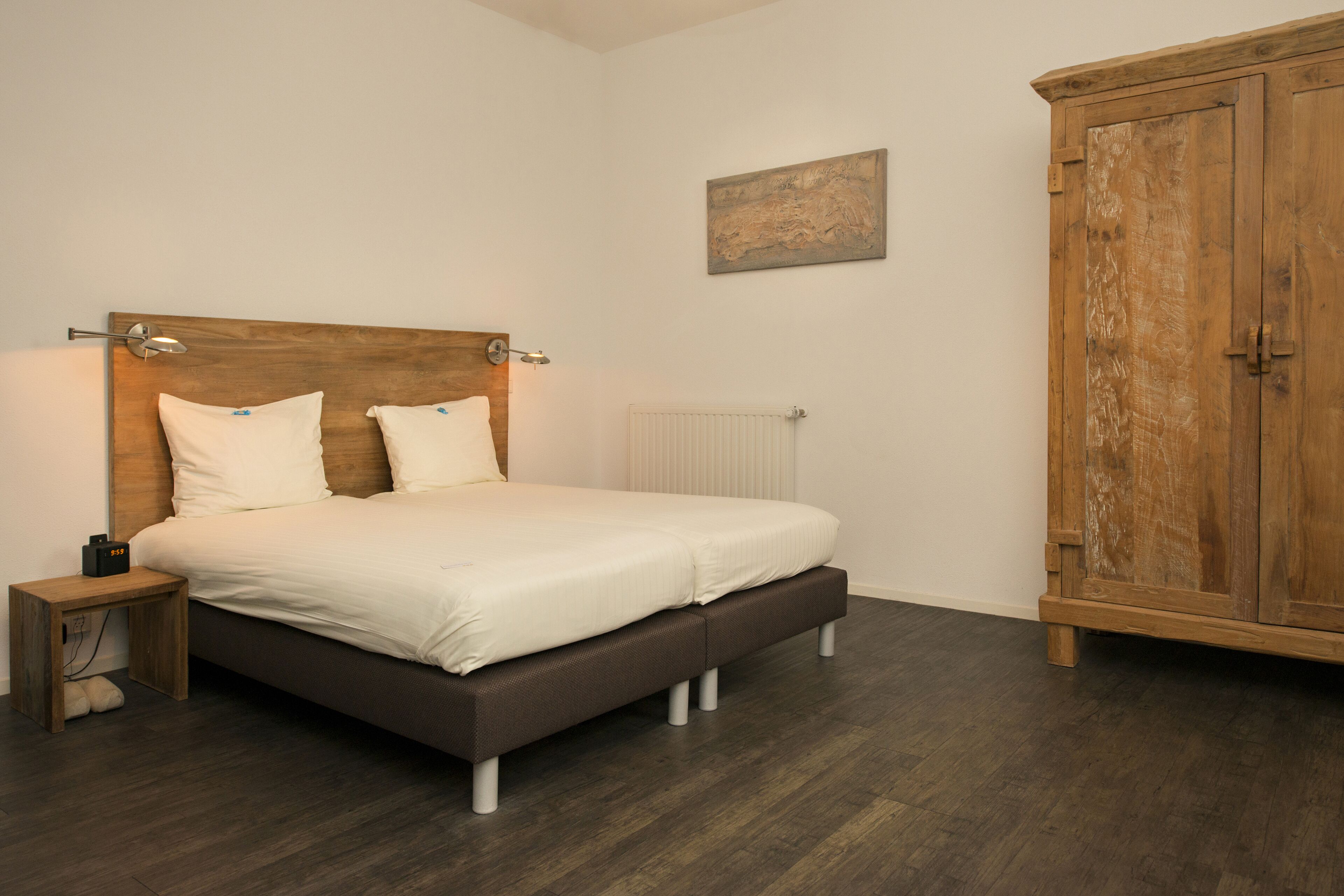 A bedroom with a wooden headboard bed, a bedside table, a radiator, and a wooden wardrobe.