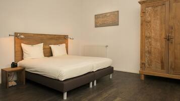 A bedroom with a wooden headboard bed, a bedside table, a radiator, and a wooden wardrobe.
