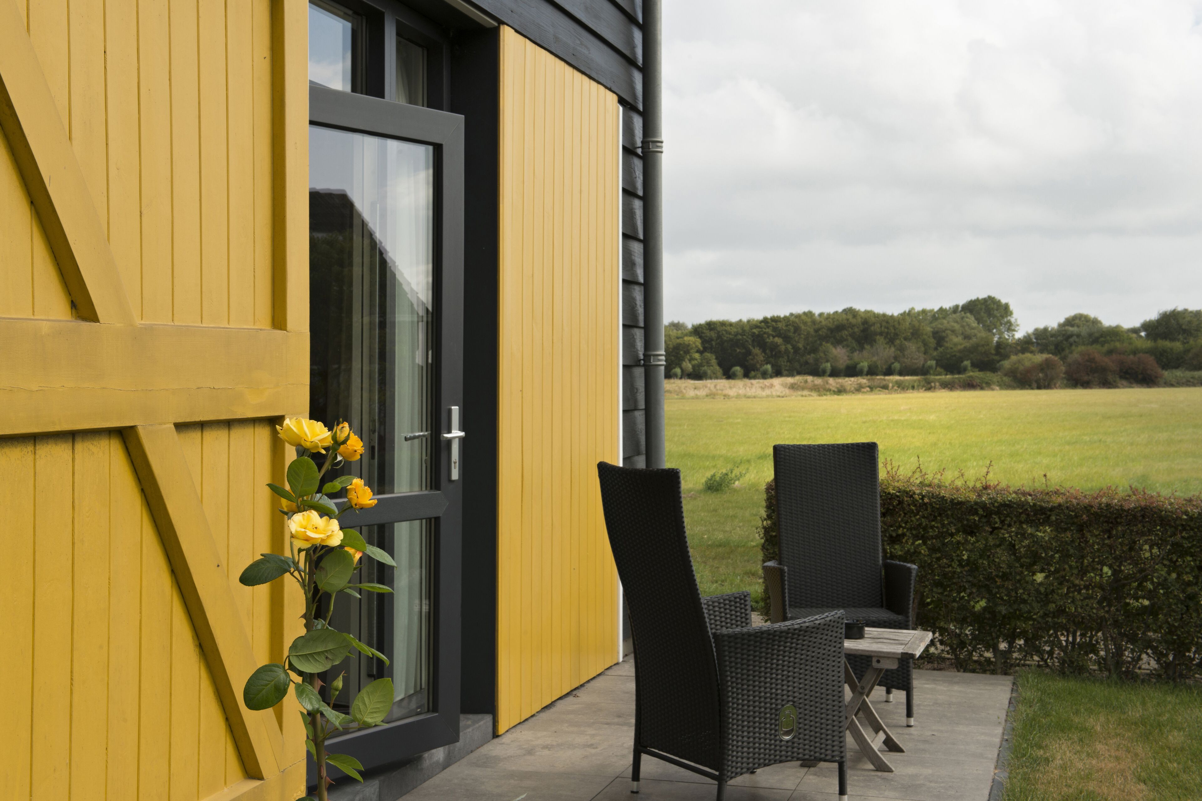 Il s’agit d’un bâtiment moderne à la façade jaune, doté d’une porte en verre. On y trouve une chaise noire et une petite table à l’extérieur.