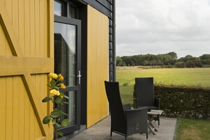 A modern building with a yellow exterior and a glass door. There is a black chair and a small table outside.