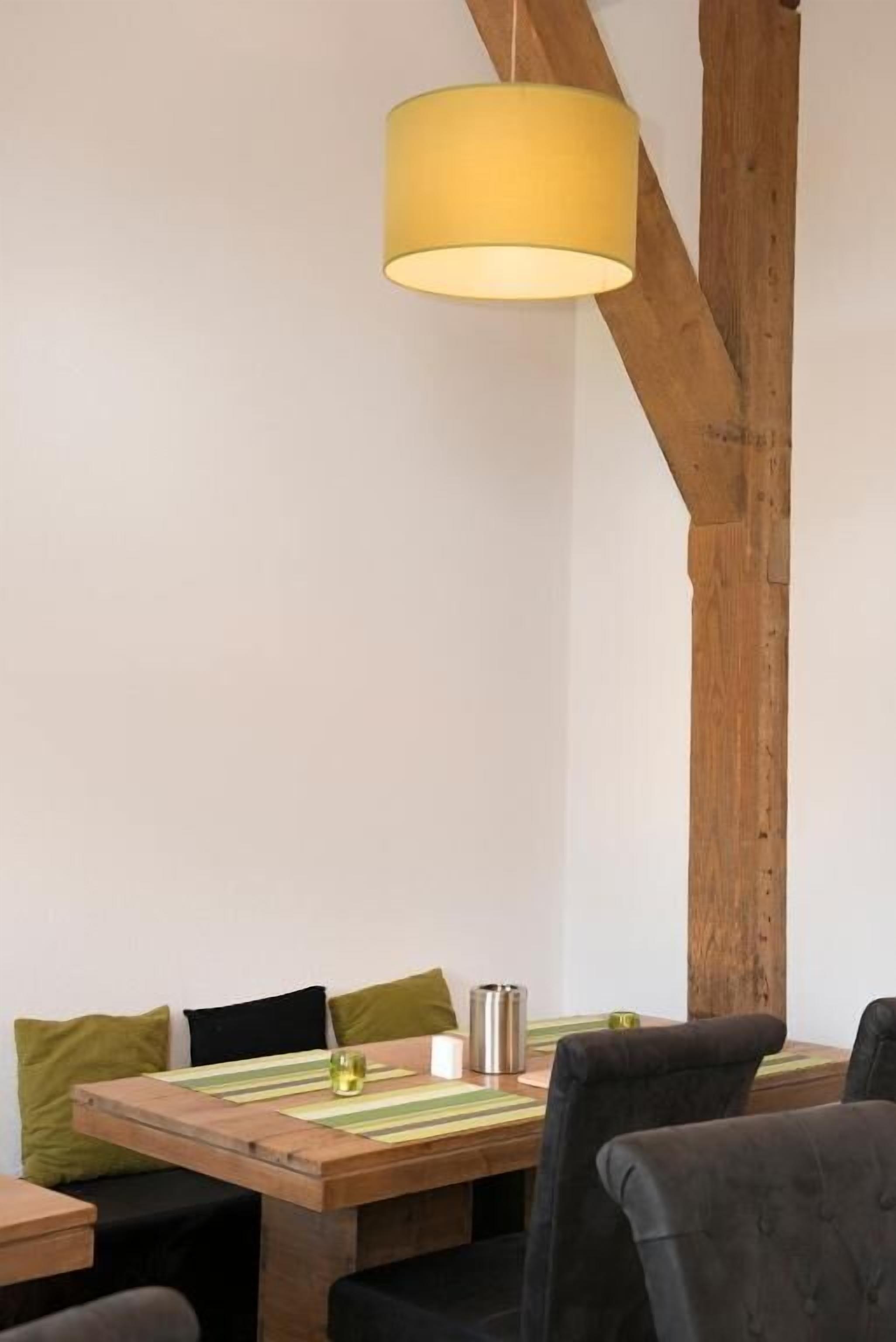 A dining area with a wooden table, chairs, and a hanging yellow lamp.