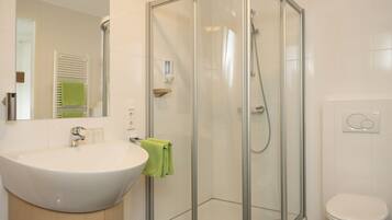 Een moderne badkamer met een douchecabine van glas, een witte wastafel en een toilet.