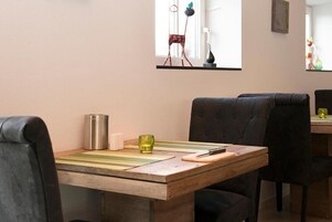 A dining area with a wooden table, black upholstered chairs, a stainless steel water bottle, a glass, and a small white object on the table.