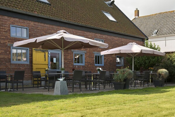 A brick building with outdoor seating, including tables and chairs, and two large umbrellas providing shade.