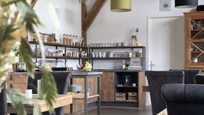 A modern kitchen with wooden beams, a dining area with black chairs, and pendant lights. - Hoevehotel Hof Christina (Vrouwenpolder)