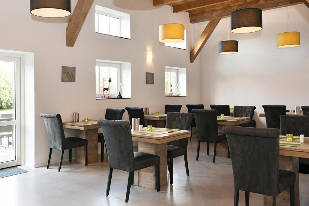 Un comedor con varias mesas y sillas, vigas de madera en el techo e iluminación colgante.