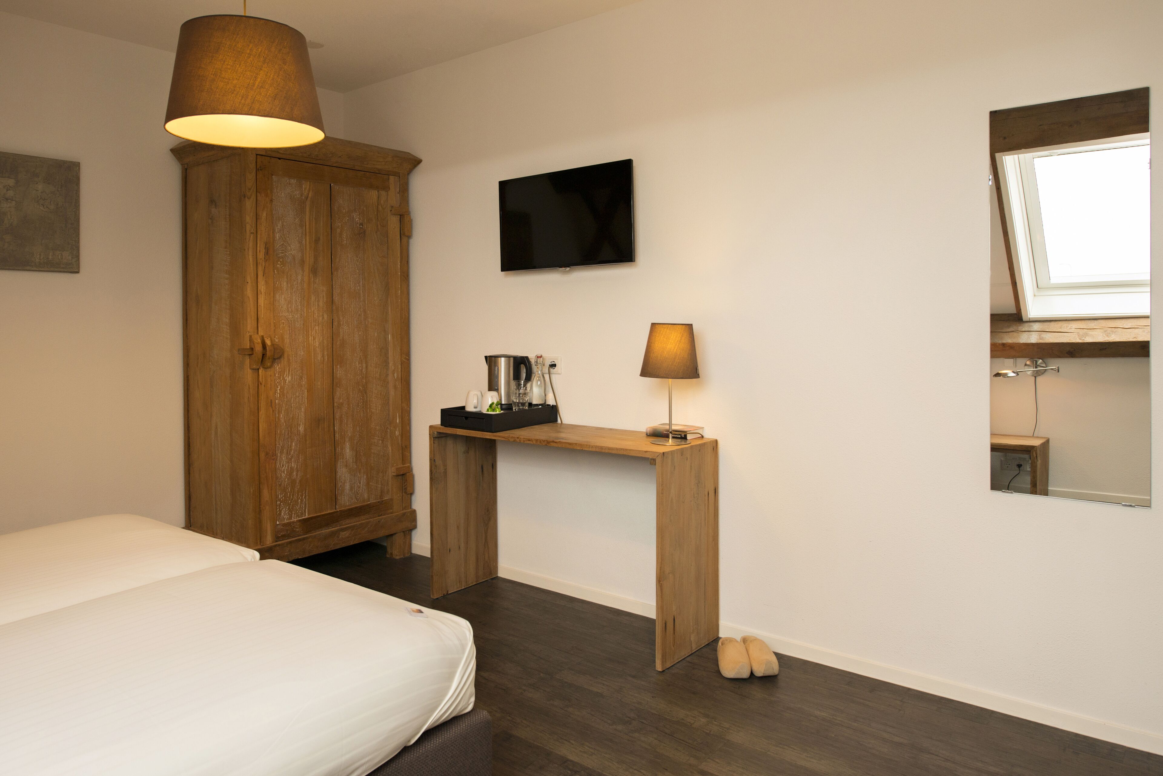 Une chambre à coucher avec un lit, une armoire en bois, un bureau avec une lampe et un téléviseur fixé au mur.