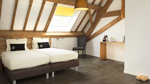 A bedroom with a sloped ceiling, wooden beams, a skylight, a bed with two pillows, a chair, and a small desk. - Hoevehotel Hof Christina (Vrouwenpolder)