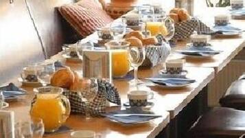 A breakfast setting with a long table set for multiple guests, featuring plates, glasses, and a pitcher of orange juice.