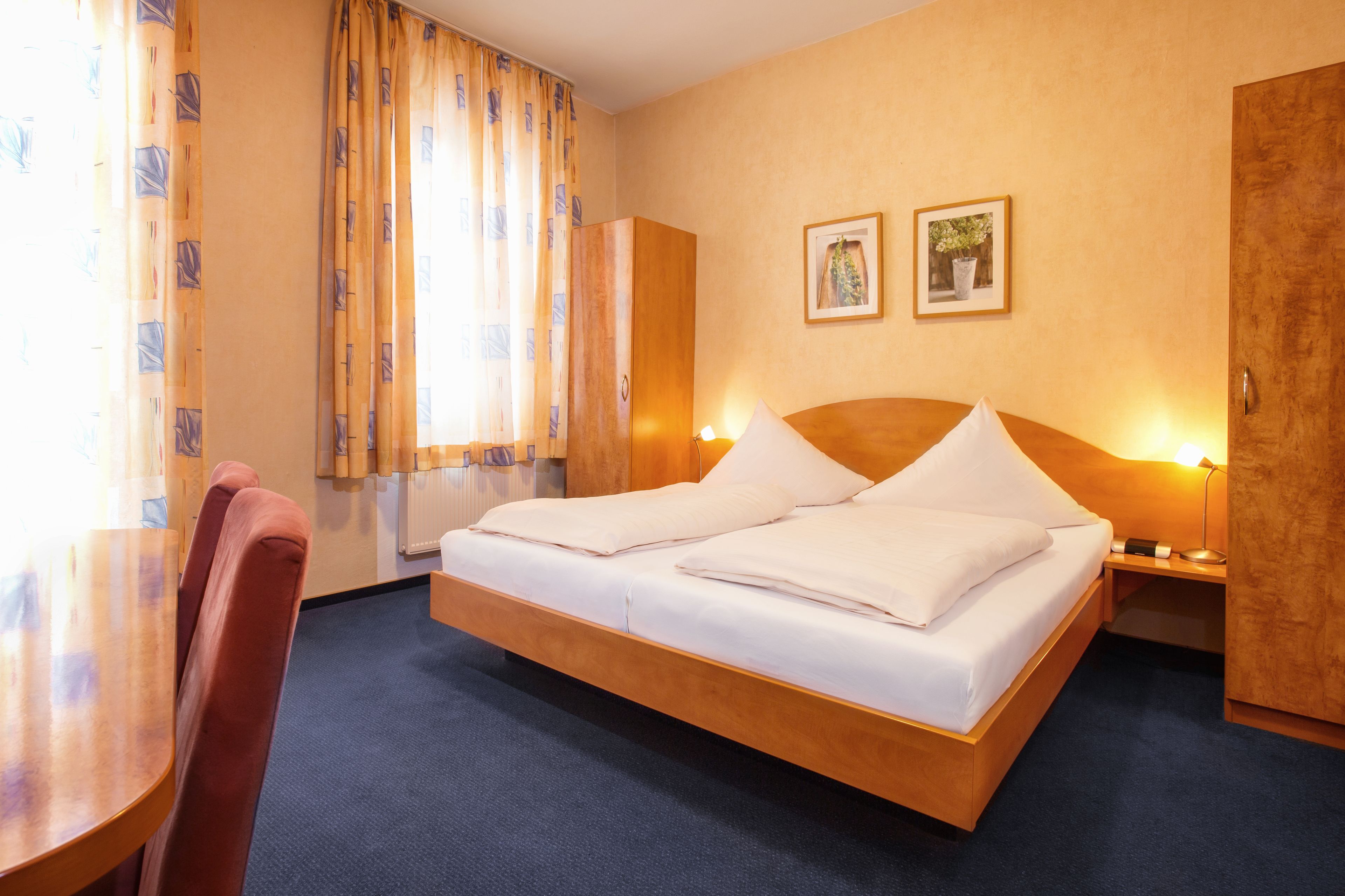Habitación de hotel con cama de madera, un escritorio y sillas. Hay dos cuadros en la pared.