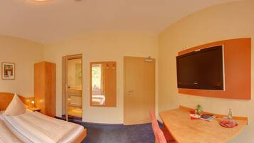 A hotel room with a bed, a desk, a chair, a television, and a bathroom visible through an open door.