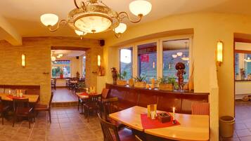 A restaurant interior with wooden tables, benches, and a chandelier.
