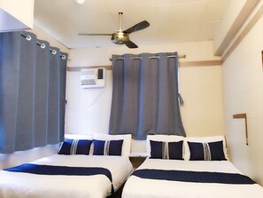 A hotel room with two beds, grey curtains, a ceiling fan, an air conditioning unit, and a white wall. - New Grand Guest House (Kowloon)