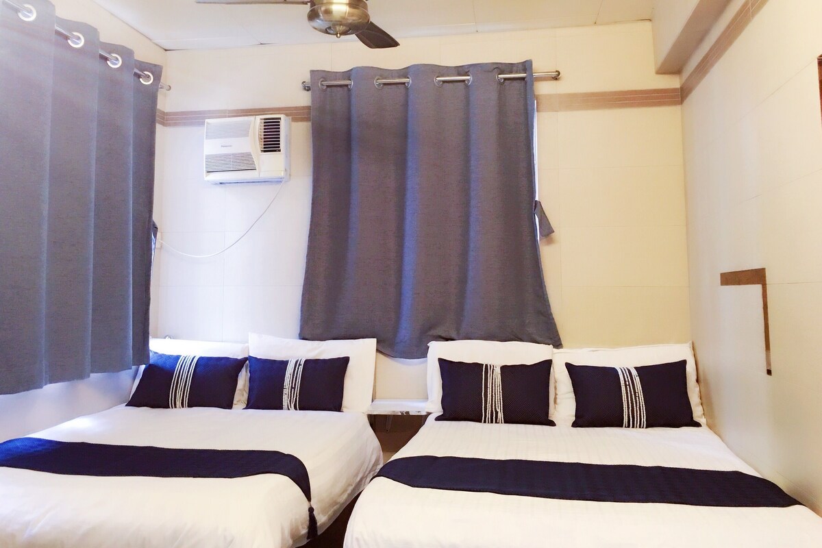 A hotel room with two beds, grey curtains, an air conditioning unit, and a ceiling fan.