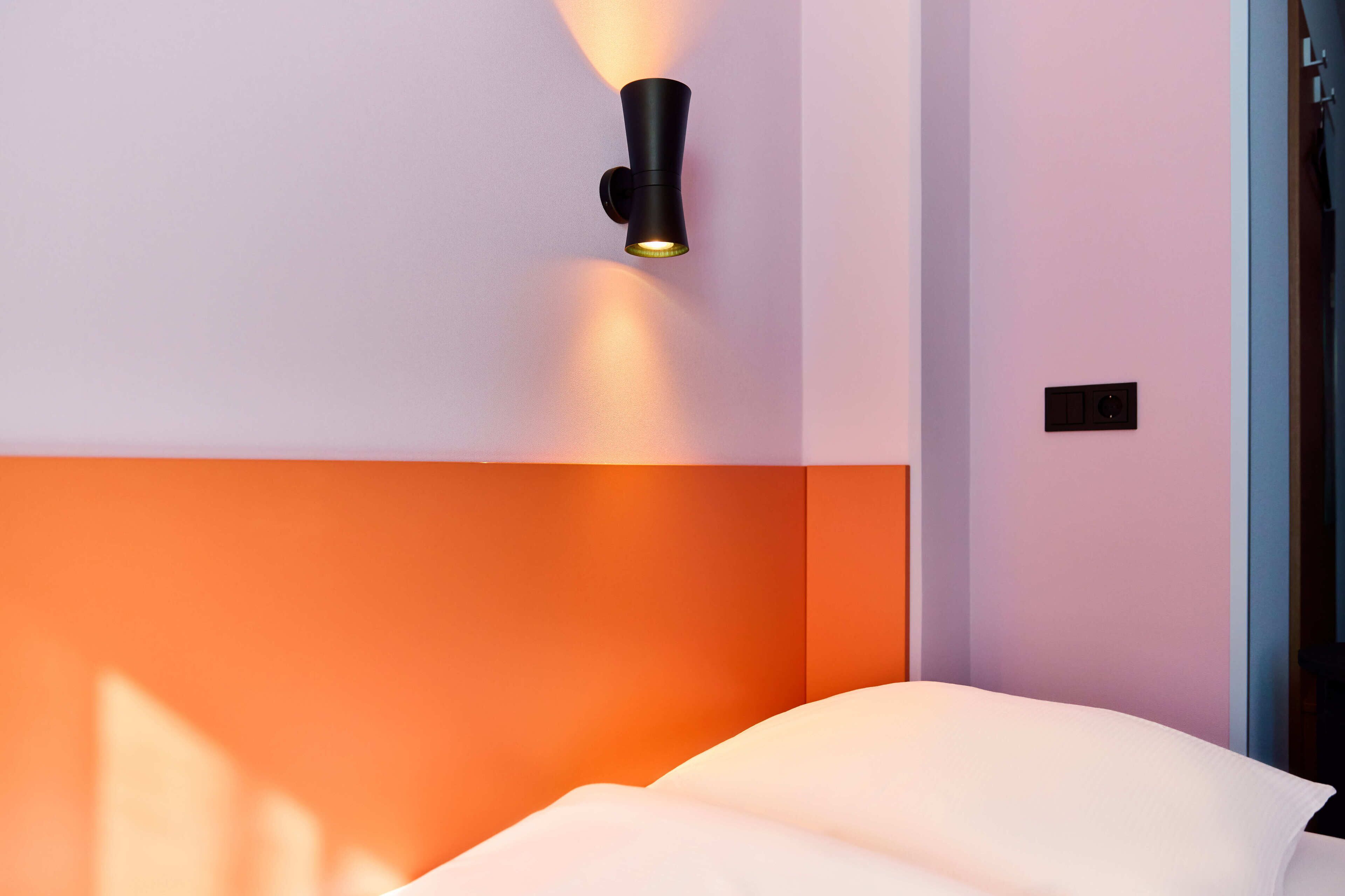 Une chambre d’hôtel moderne, équipée d’un lit, d’un luminaire fixé au mur et d’une porte.