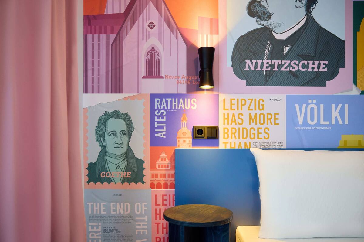 Una habitación con un sofá azul, un taburete de madera redondo y una pared decorada con varios carteles y una lámpara.