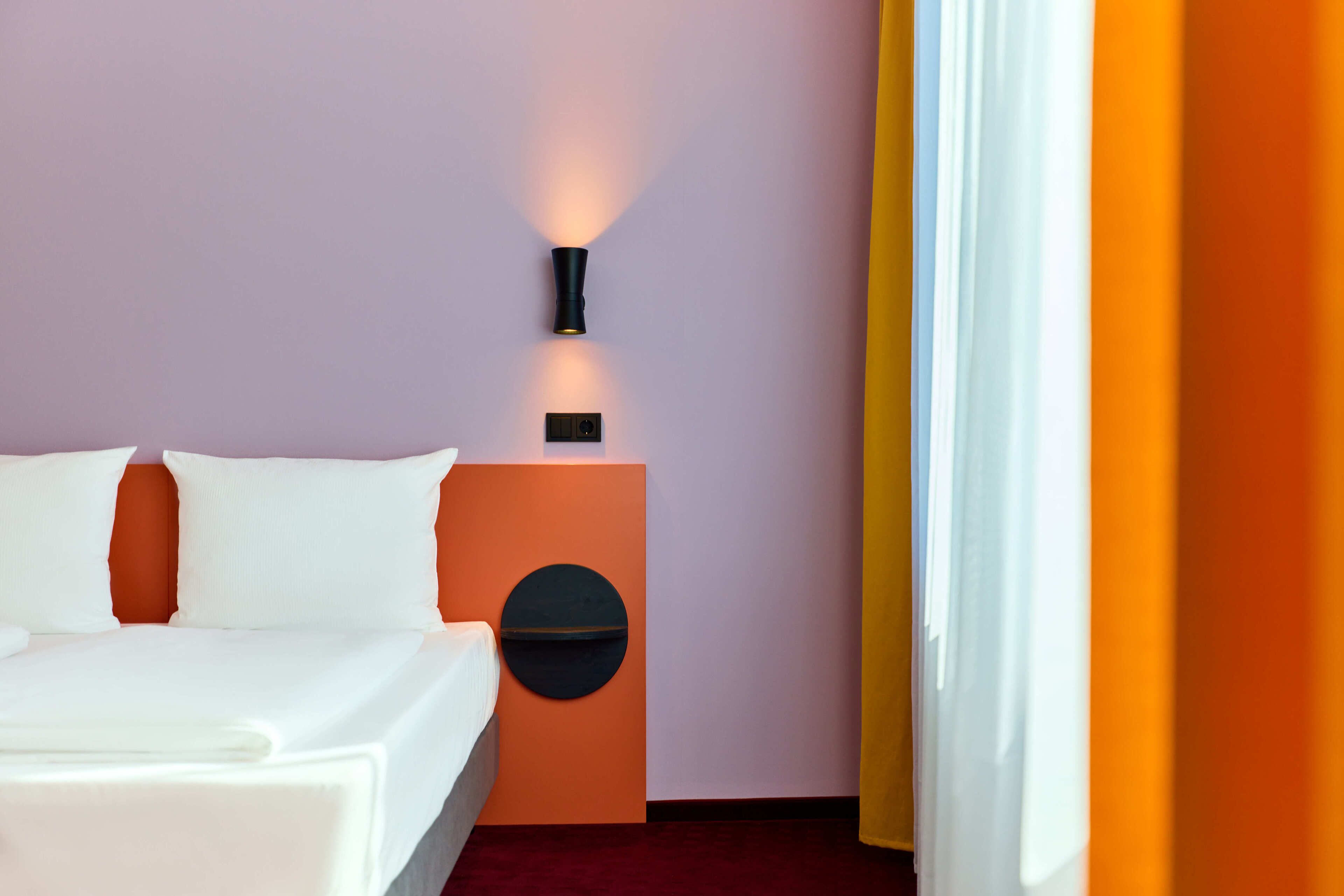 Une chambre d’hôtel avec un lit, une table de chevet avec une lampe et un élément décoratif circulaire fixé au mur.