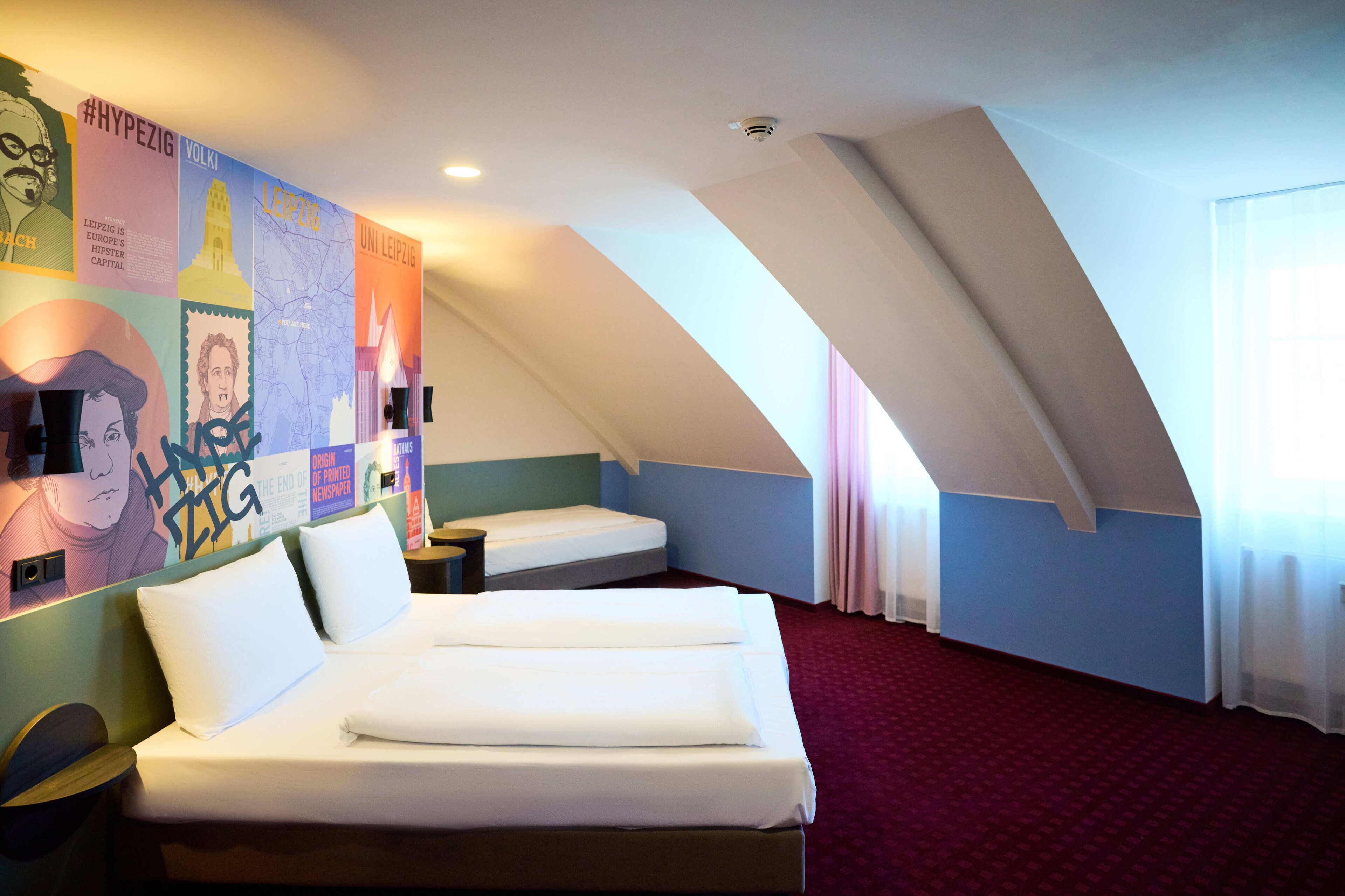 A hotel room with two beds, a red carpet, and a sloped ceiling with a skylight.