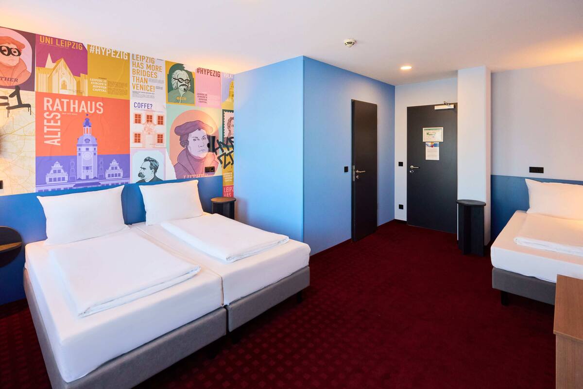 Habitación de hotel con dos camas, alfombra roja y una pared decorada con varios carteles.