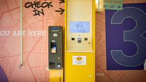 Un kiosque d’enregistrement automatisé avec une carte et des panneaux indicateurs, notamment un panneau indiquant « CHAMBRES ZIMMER » et un grand chiffre « 3 » sur le mur.