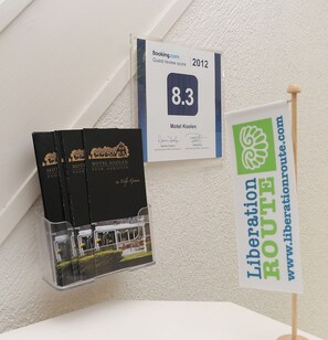 Eine Gästebewertung von 8,3 für das Motel Koolen, ein Schild für die Befreiungsroute und drei schwarze Bücher mit dem Titel 'Motel Koolen'.