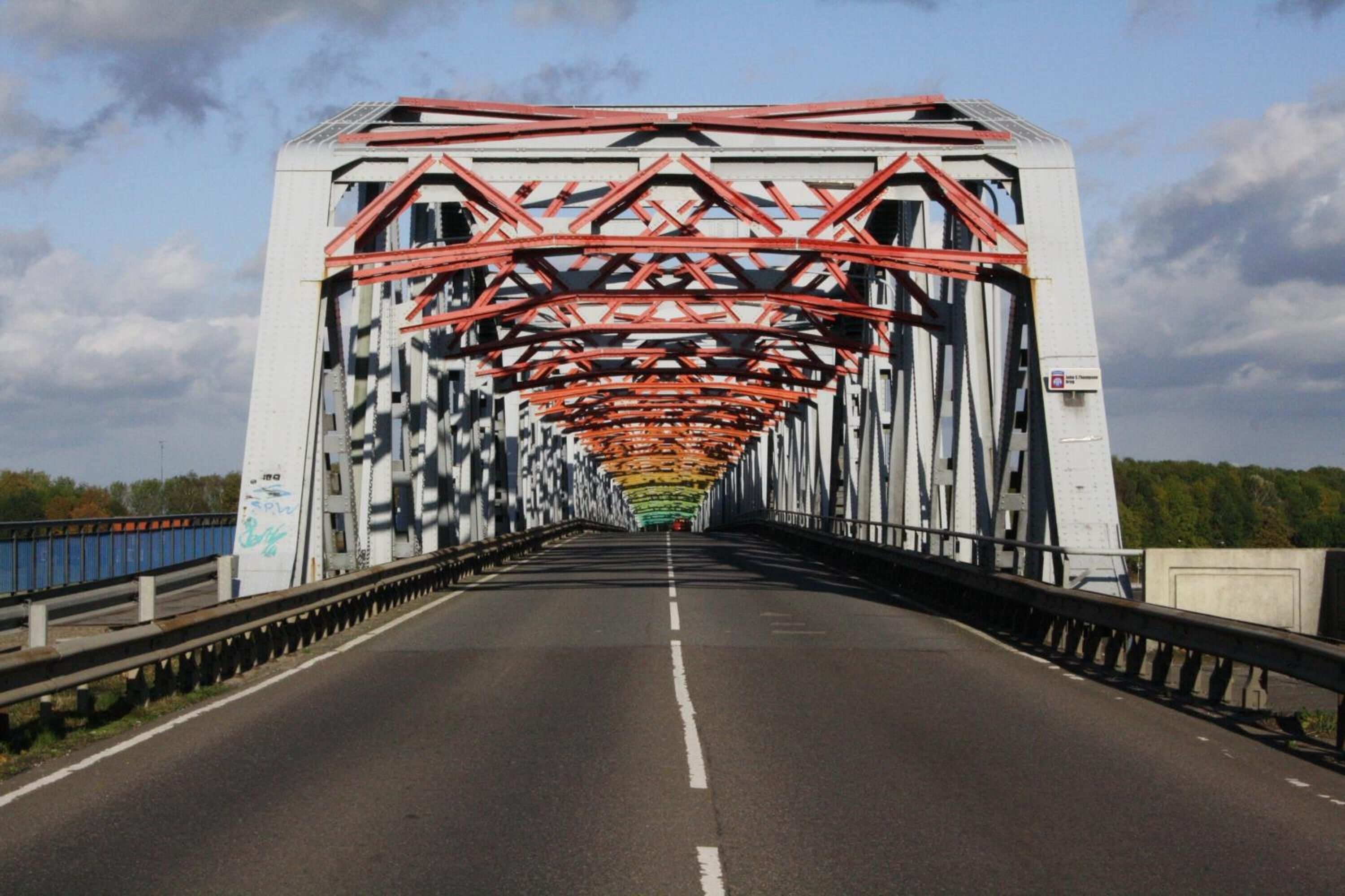Eine Brücke mit einer weißen und roten Metallkonstruktion, einem klaren Himmel und einer Straße mit weißen Fahrbahnmarkierungen.