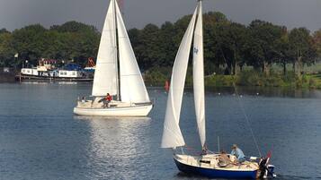 Two sailboats on a calm lake with a docked boat in the background and trees along the shore.