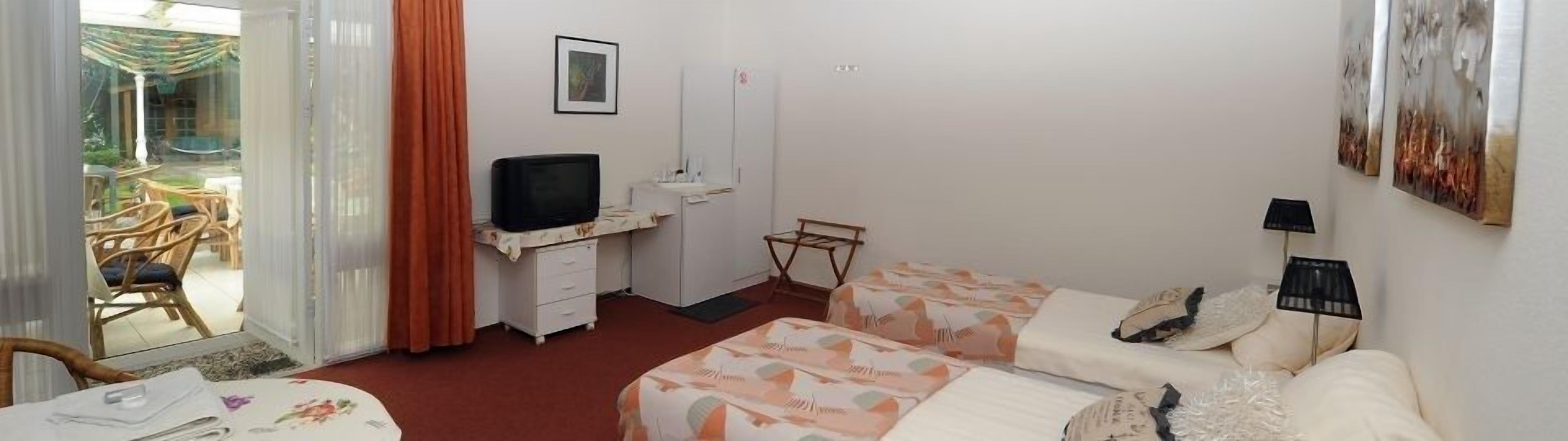 A hotel room with a bed, a desk with a television, a chair, a small table, and a window with curtains.