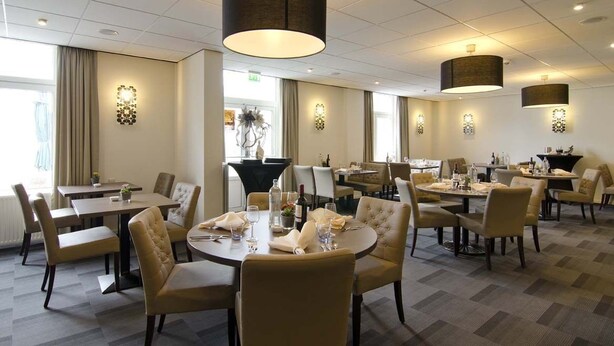 Ein Hotel-Essbereich mit mehreren Tischen und Stühlen, Pendelleuchten und dekorativen Wandleuchten.