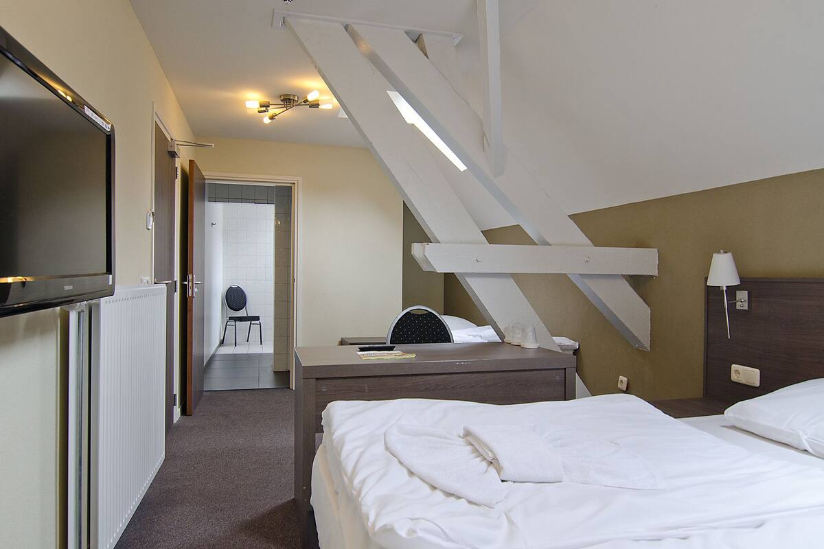 A hotel room with a bed, a desk, a chair, a TV, and a staircase.