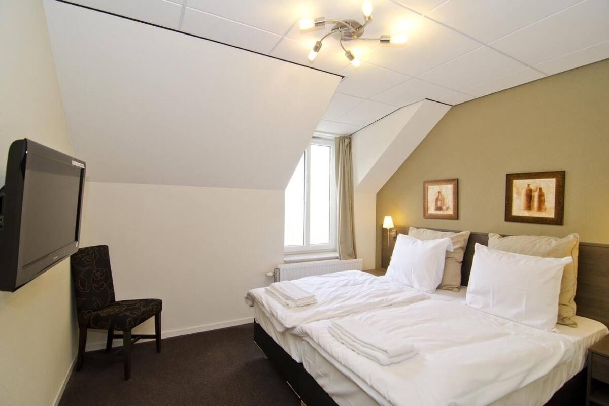 A hotel room with a bed, a chair, a TV, and a window.