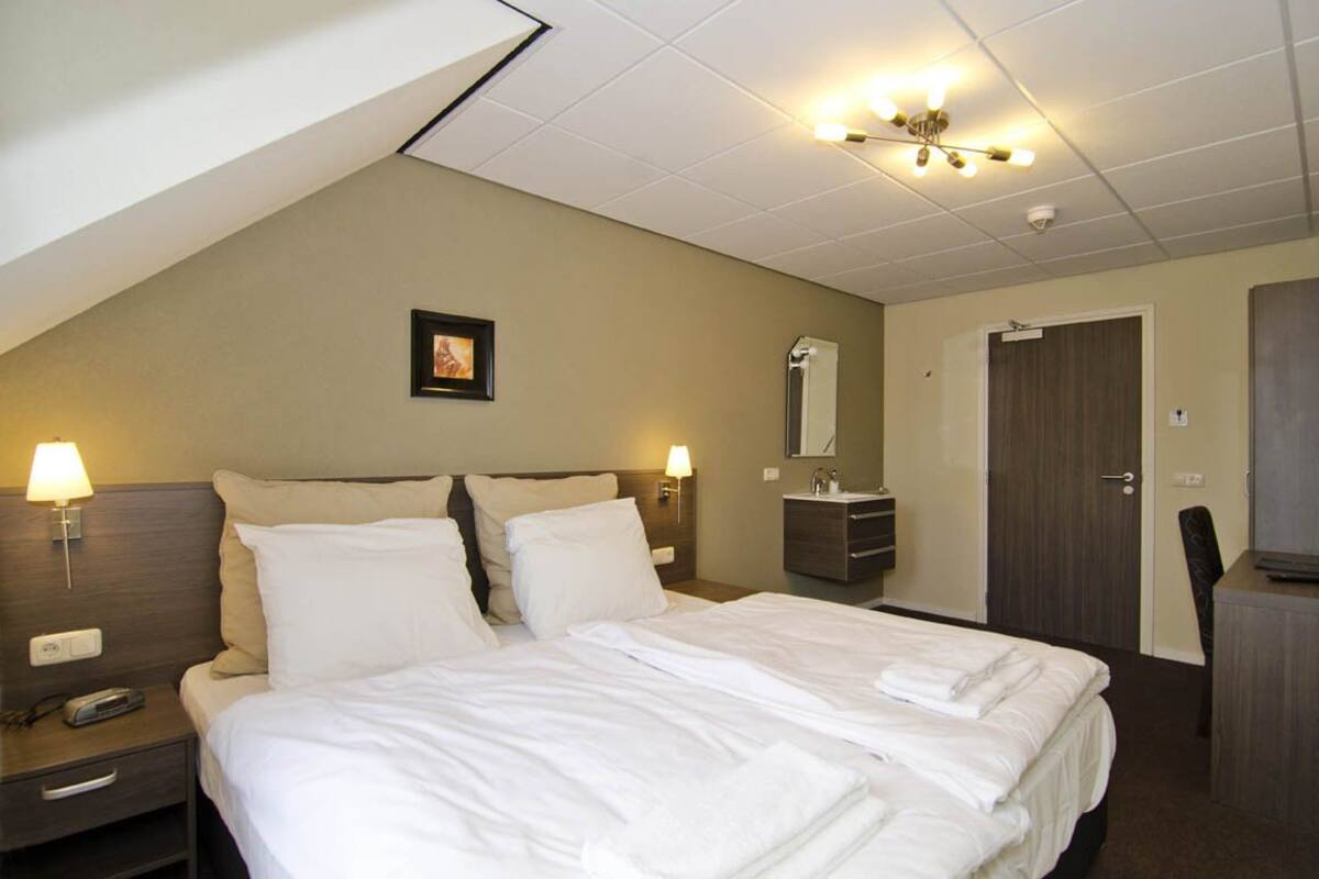 A hotel room with a large bed, bedside lamps, a mirror, a dresser, and a door.