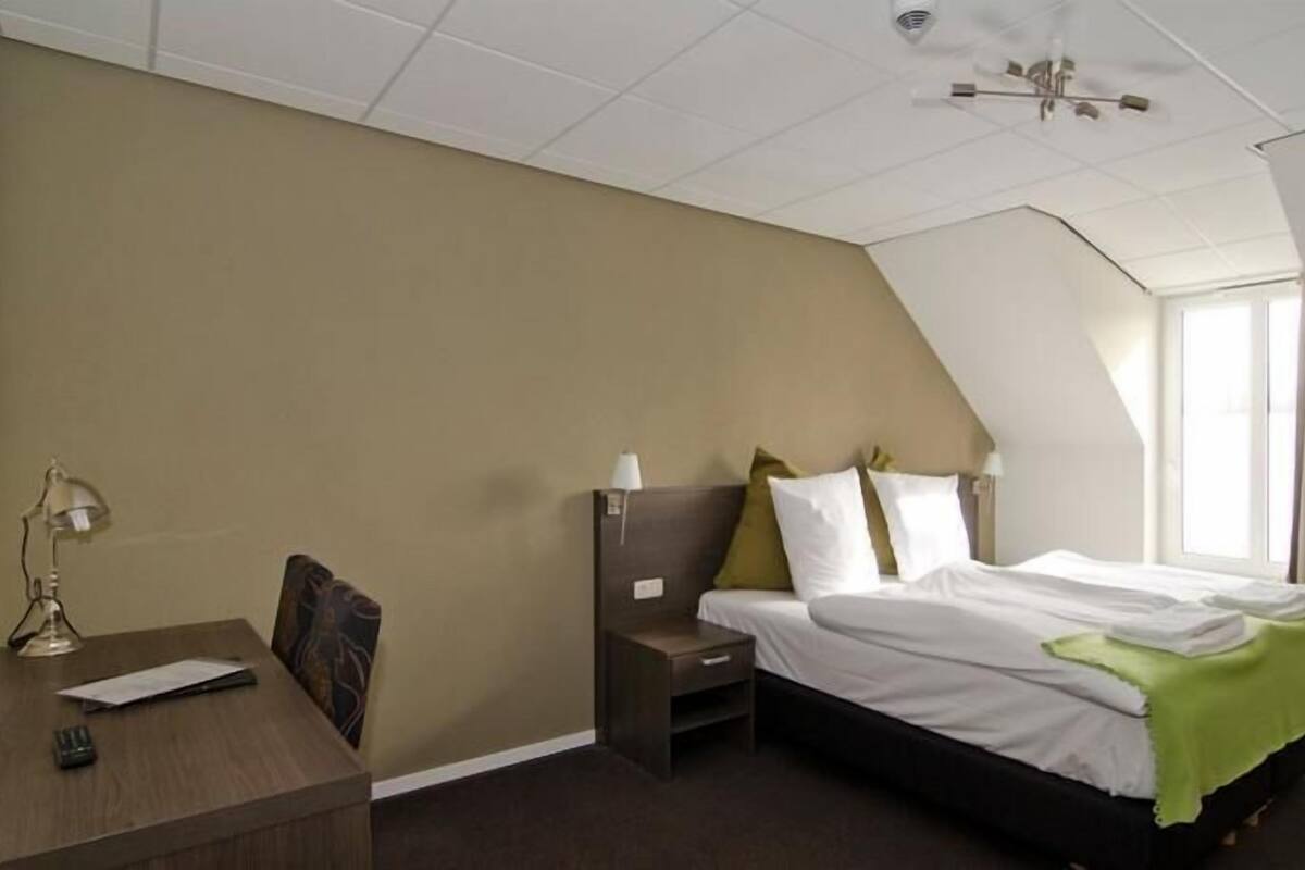 A bedroom with a bed, a desk, a chair, and a nightstand.
