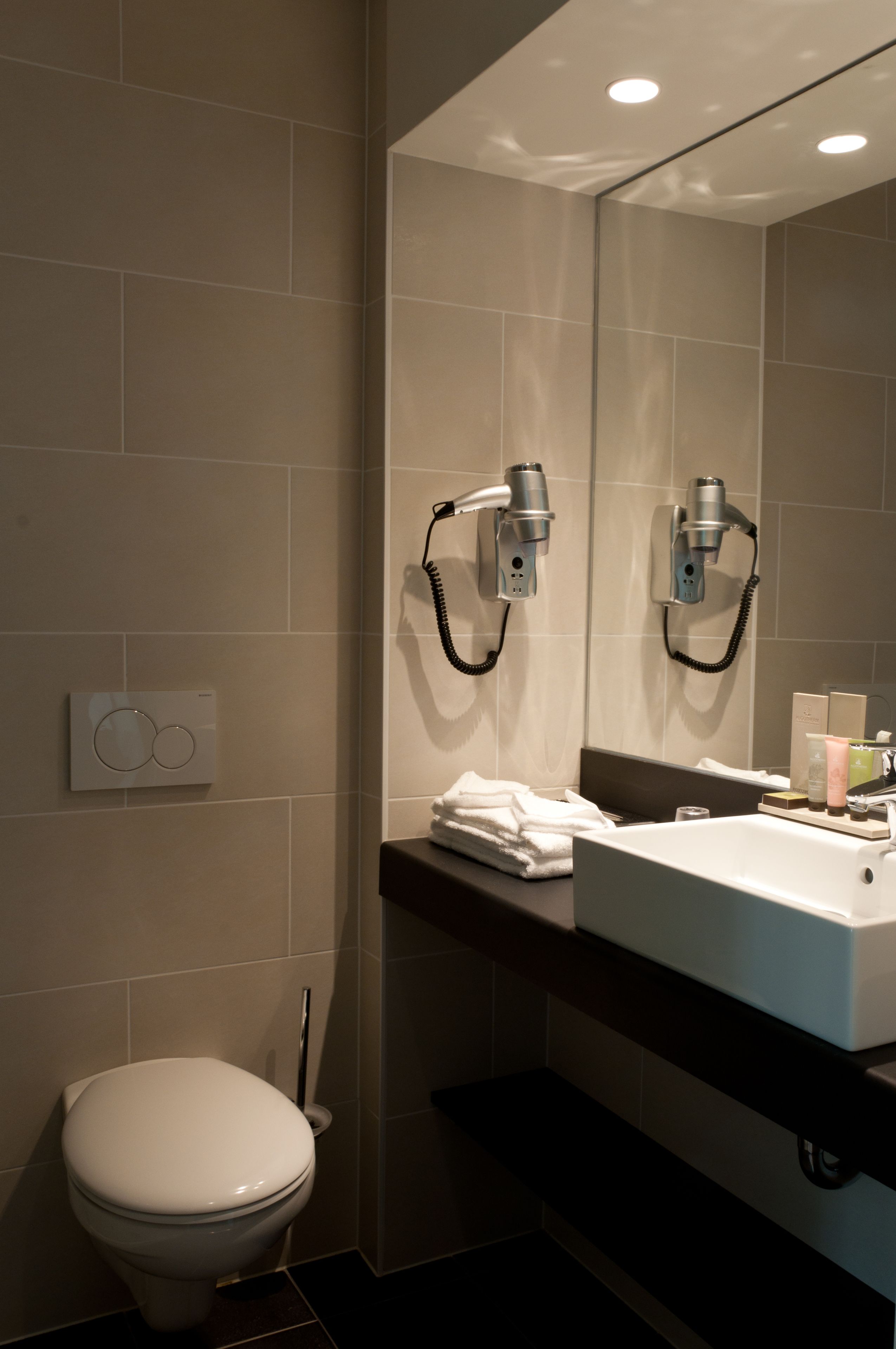 A modern bathroom with a toilet, a sink, and a hairdryer mounted on the wall.