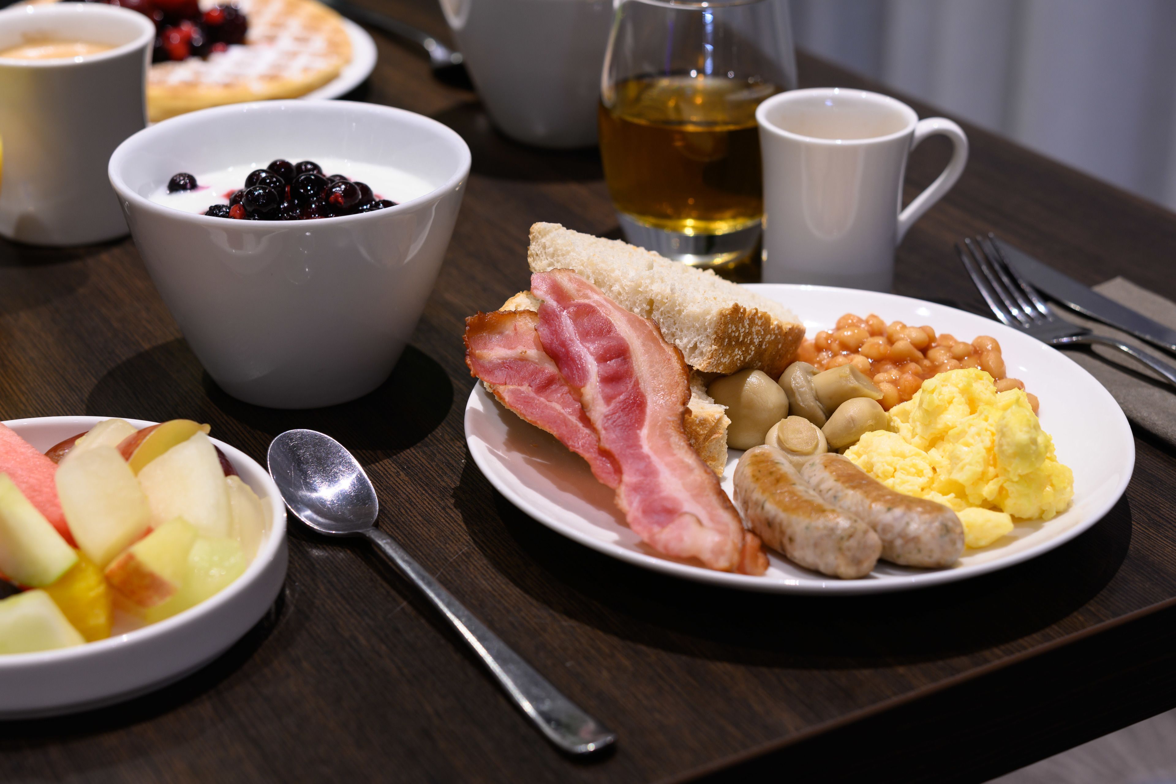 Una mesa de desayuno con un plato de huevos, salchichas, frijoles y tostadas.
