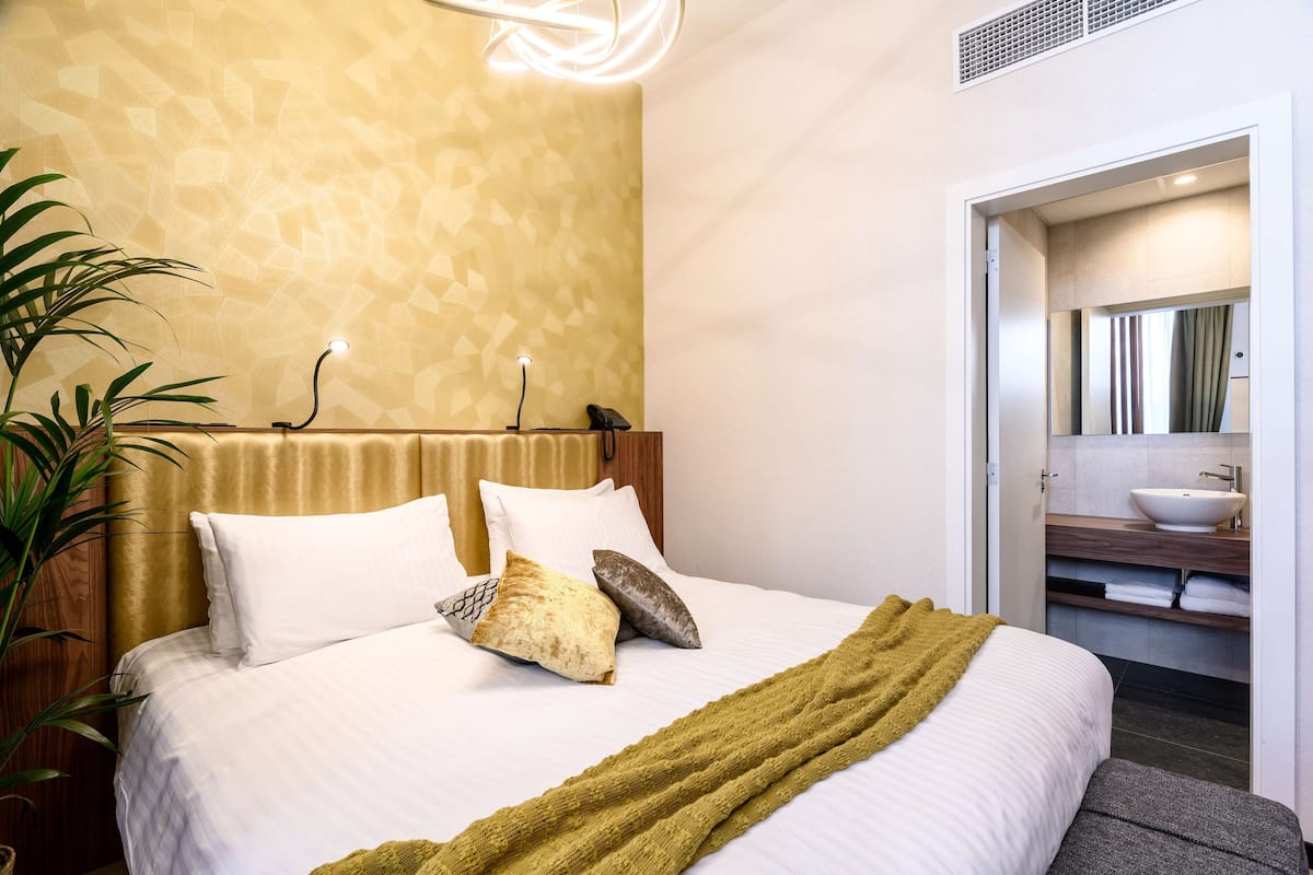 A neatly made bed with a green throw blanket, a bedside plant, and a modern headboard.
