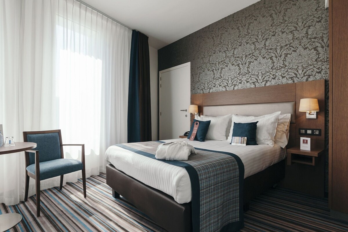 A hotel room with a bed, a chair, a bedside table, and a nightstand.