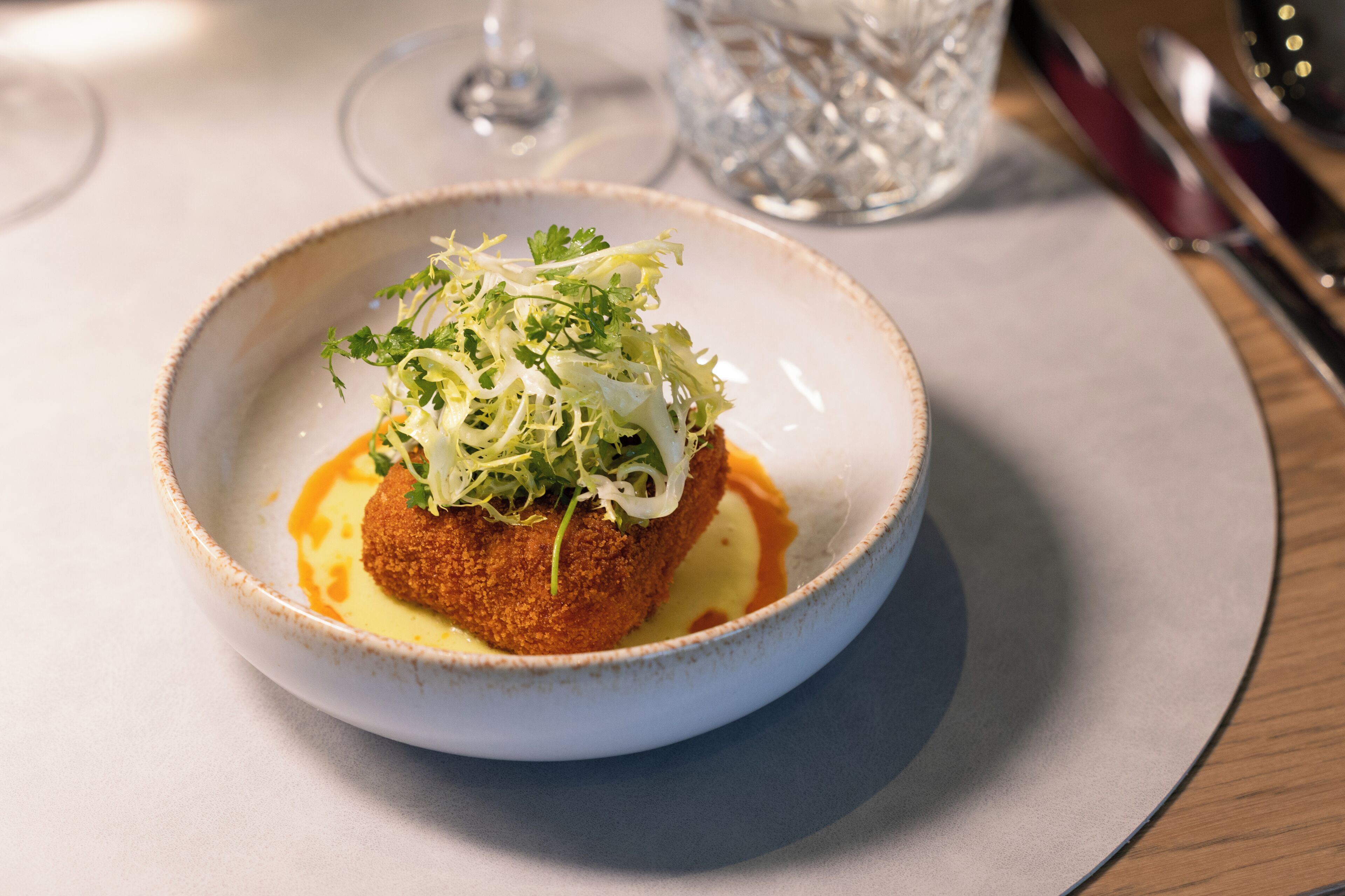 Un plat servi dans une assiette en céramique, accompagné d’un verre d’eau et de couverts placés sur la table.