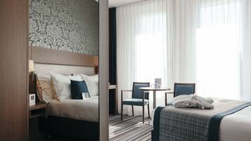 Une chambre d’hôtel avec un lit, une chaise, une petite table et une fenêtre avec des rideaux.