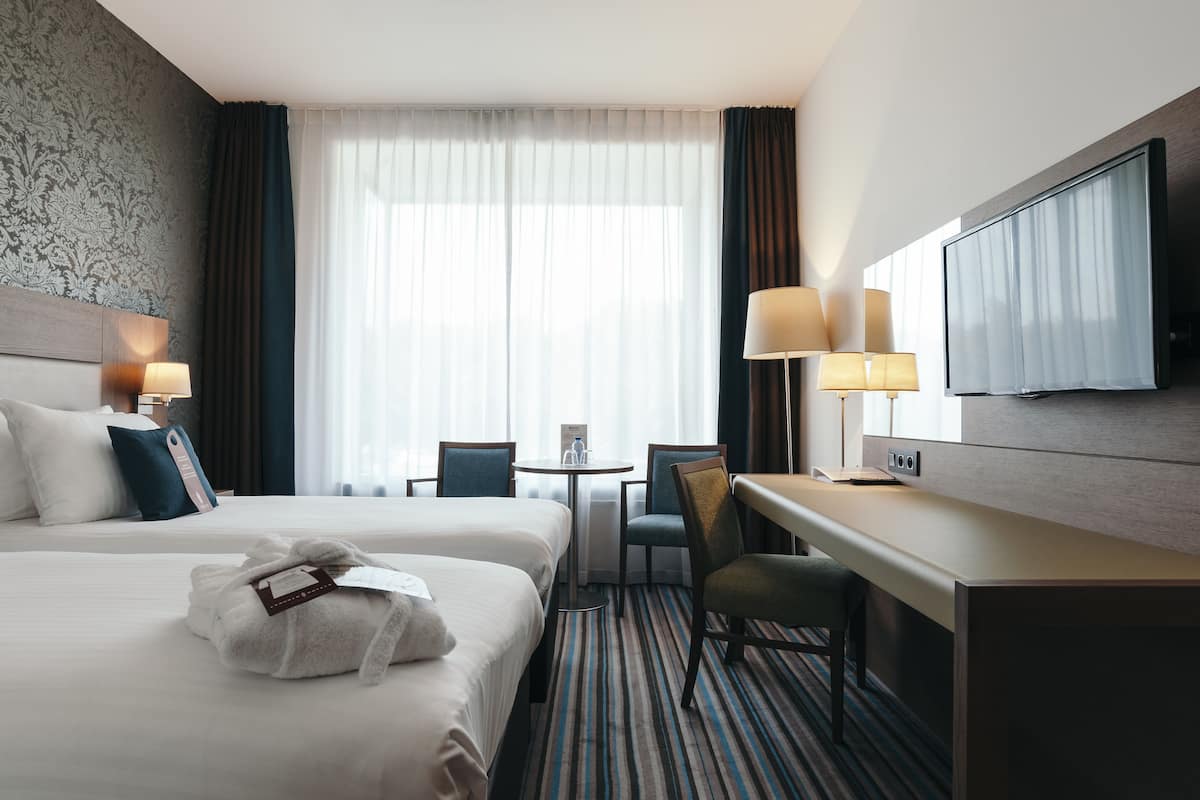 A hotel room with two beds, a desk, a chair, a television, and a window with curtains.