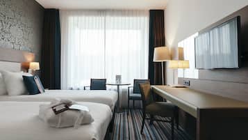 Hotelkamer met twee bedden, een bureau, een stoel, een televisie en een raam met gordijnen.