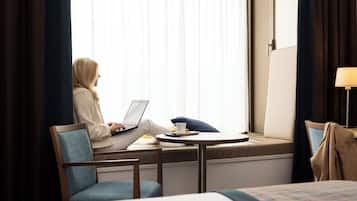Habitación de hotel con cama, un asiento junto a la ventana con una computadora portátil, una taza y una almohada.